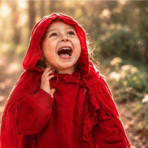 Little girl in a red cloak laughing in the woods